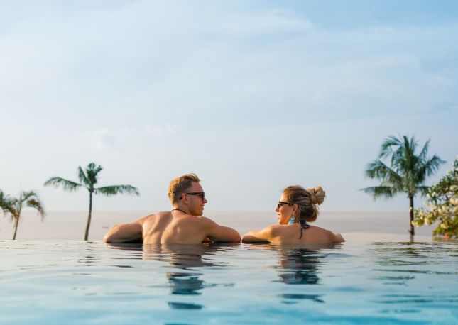 a man and woman with their back to the camera sitting in an infinity pool.